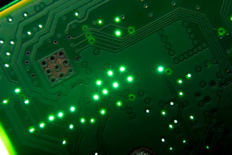 Backlit FR-4 PCB highlighting vias and trace routing under green solder mask.