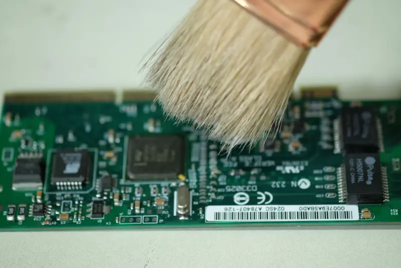 nti-static brush cleaning a populated PCB before rework—dust removal step in PCB assembly design for higher reliability.