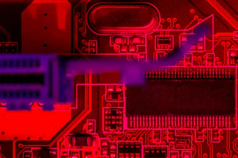 Substrate Material Selection: red-lit macro of a PCB showing microcontroller, crystal can, and copper traces with a blurred blue connector in the foreground.